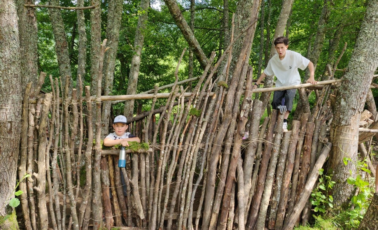 Enfants apprenant à construire leur cabane en forêt lors d'une colonie de vacances nature